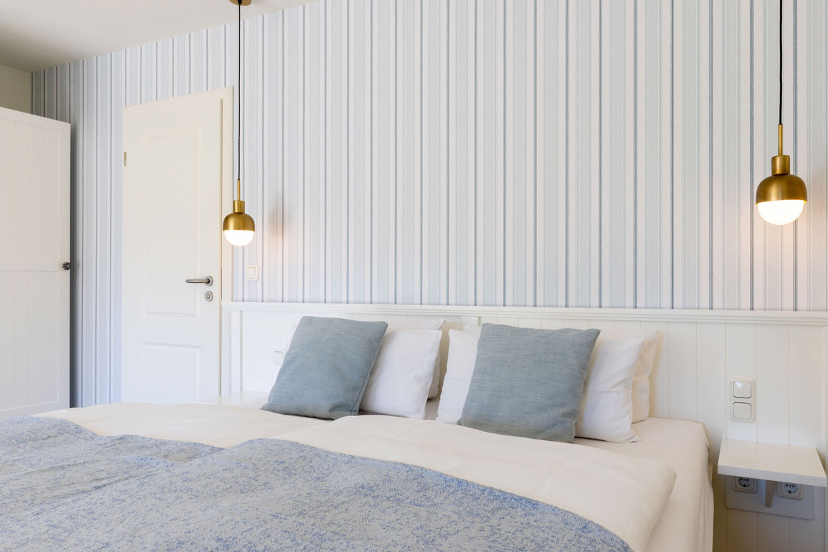 Doppelbett im Terrassenzimmer des STRANDHAUS Ahrenshoop mit blau-weißer Streifentapete und goldenen Pendelleuchten.